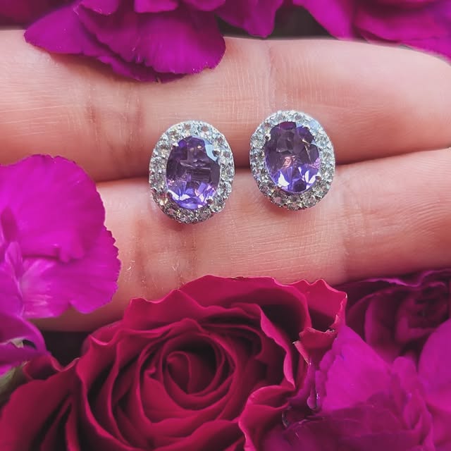 A pair of Brazilian amethyst earrings haloed in white topaz, photographed above a deep magenta carnation.