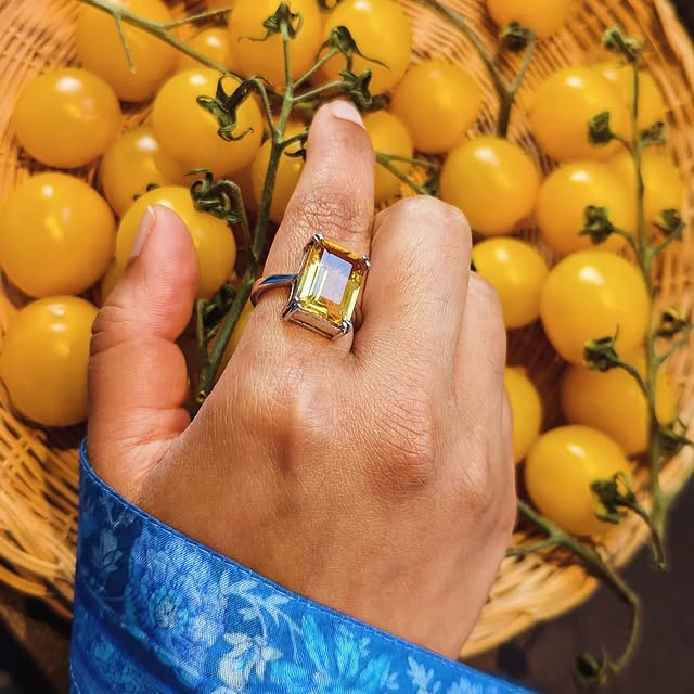 An emerald-cut Madagascar citrine ring in fine silver, resting on a hand above a basket of sungold tomatoes.