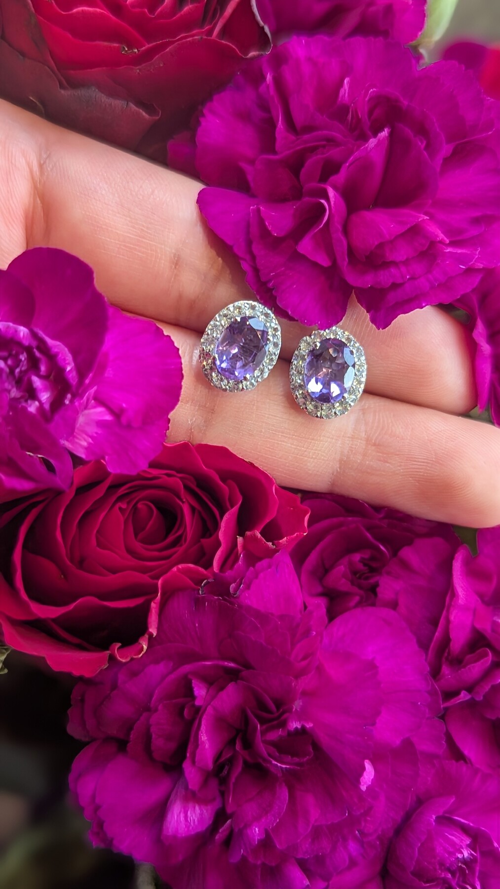 Amethyst earrings with white topaz held among pink and red flowers.