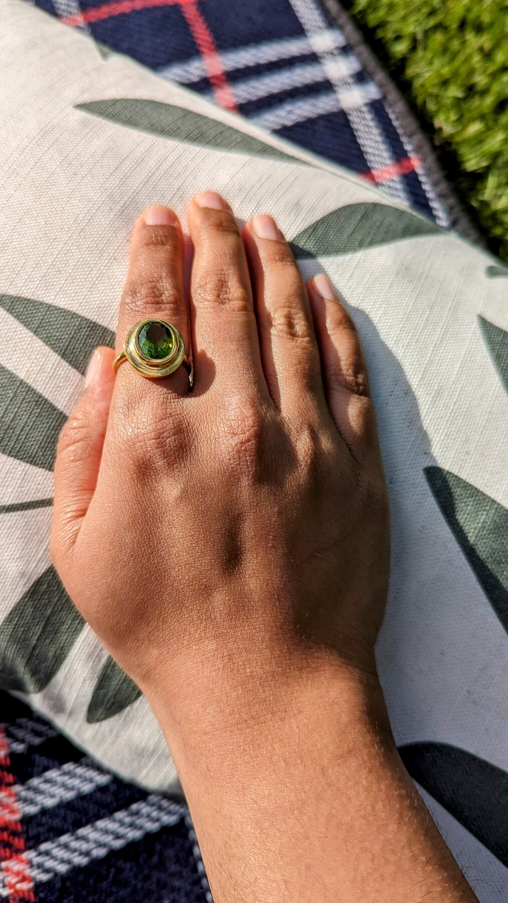 Peridot ring worn in sunlight on a patterned cushion.