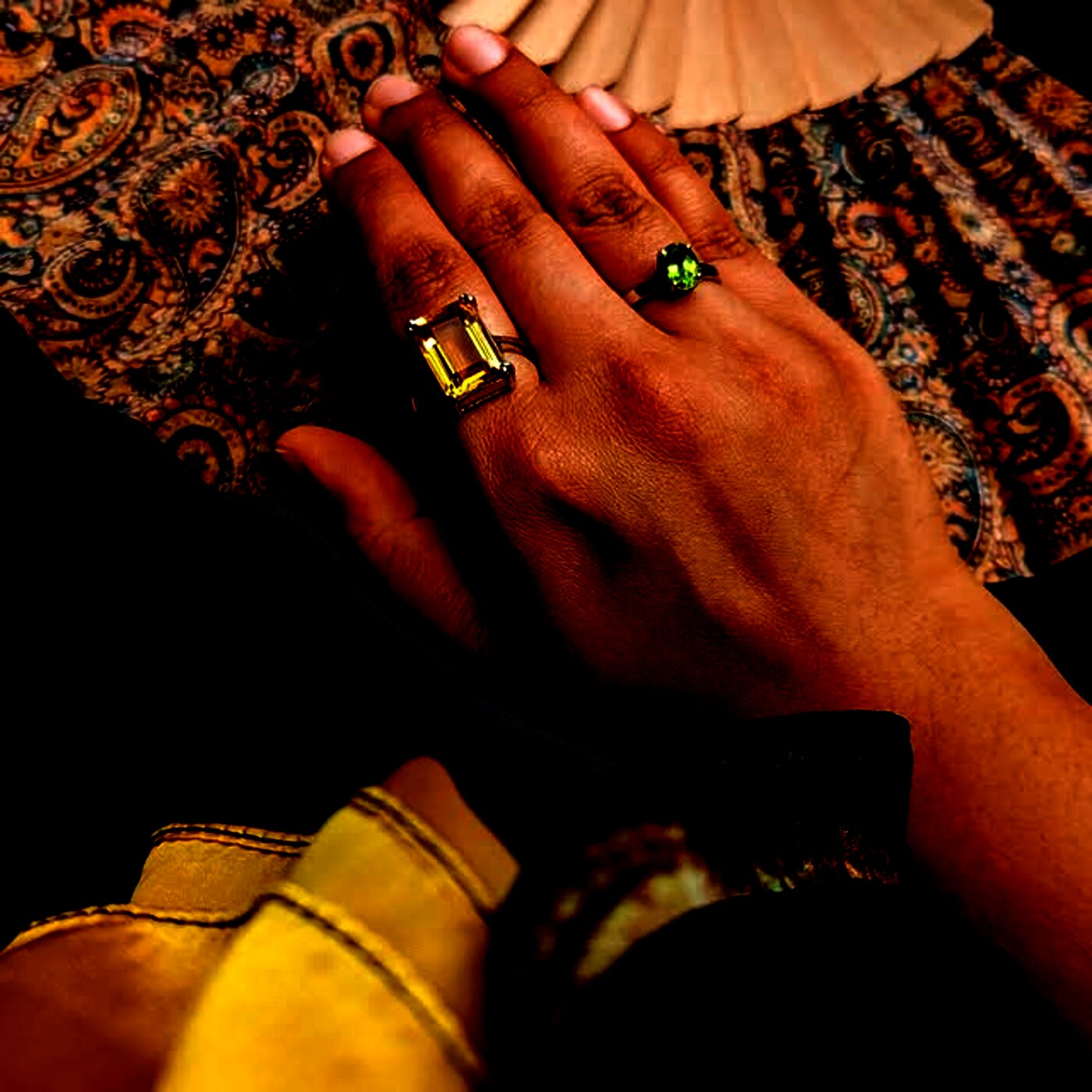 An emerald-cut citrine ring and an oval peridot ring worn together, resting on warm paisley silk.